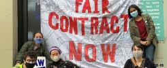 Banner that reads "Fair Contract Now" hung on a building with a group of graduate students on the picket surrounding it